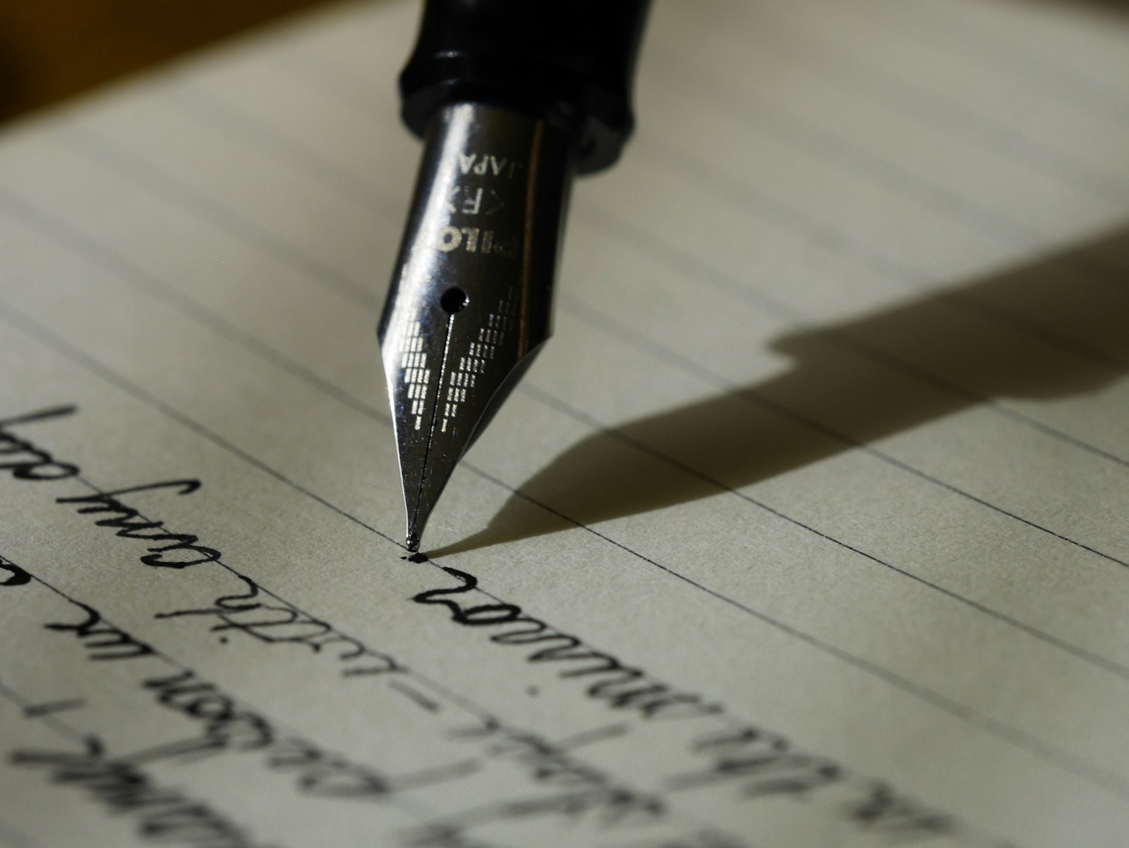 A fountain pen nib writing a line of cursive in black ink on ruled cream paper